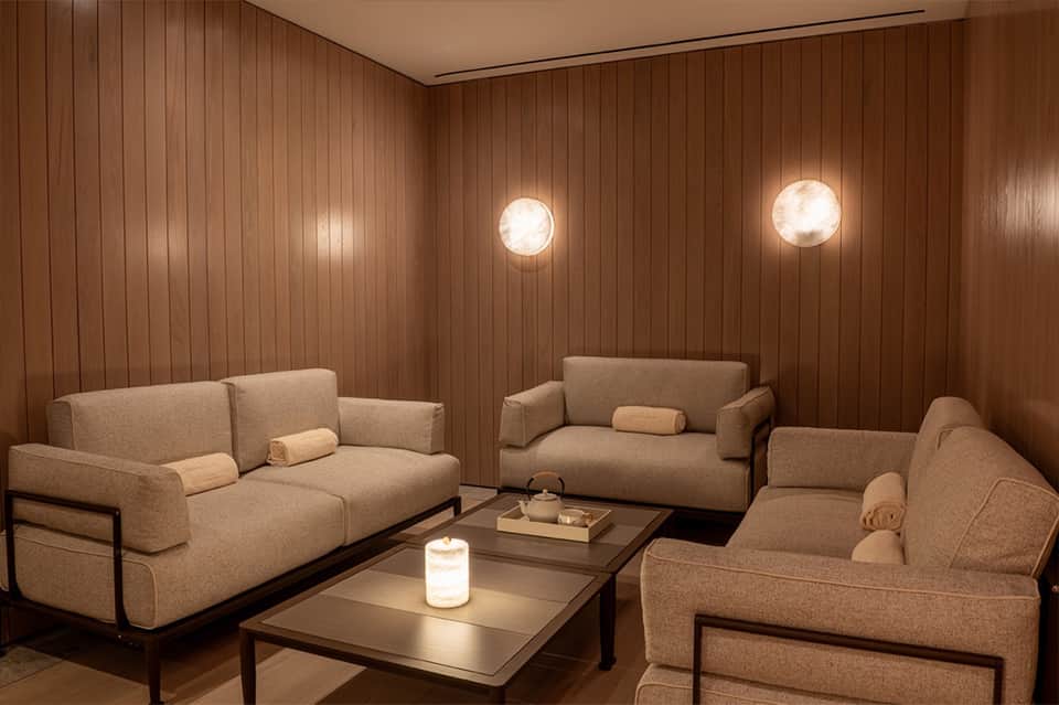 Warm wood-paneled lounge with three upholstered sofas, round tables, and recessed ceiling lights