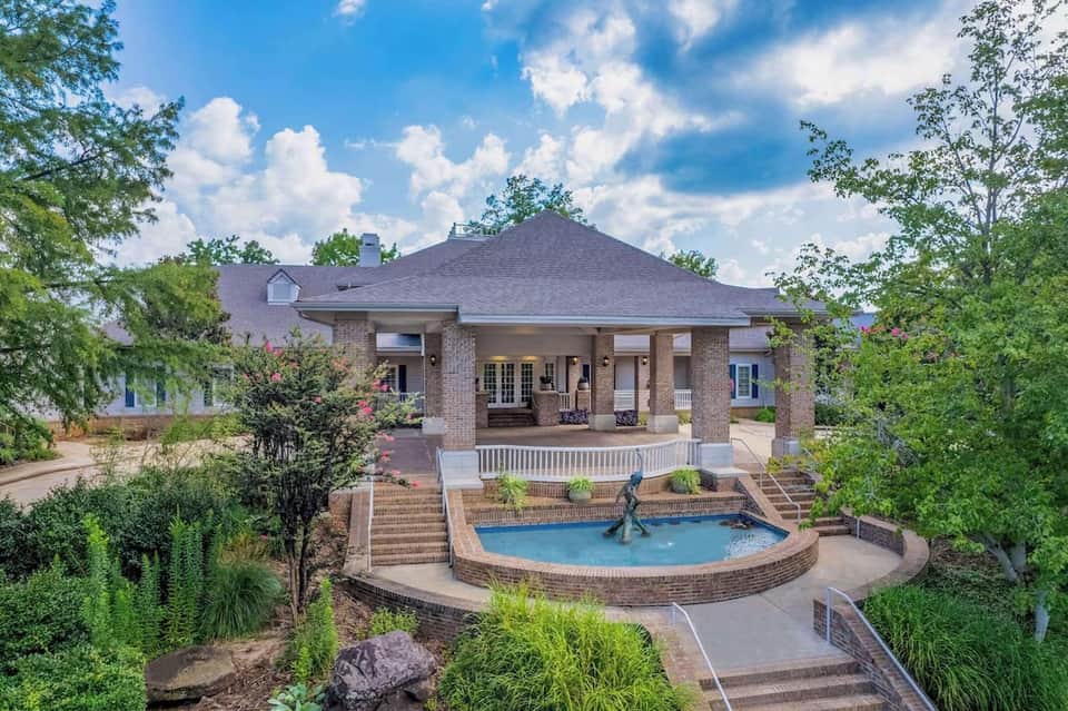 Brick mansion with columned porch, circular spa pool, and manicured landscaping