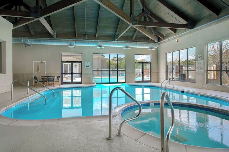 Indoor heated swimming pool with exposed wooden ceiling beams, large windows, and spa hot tub