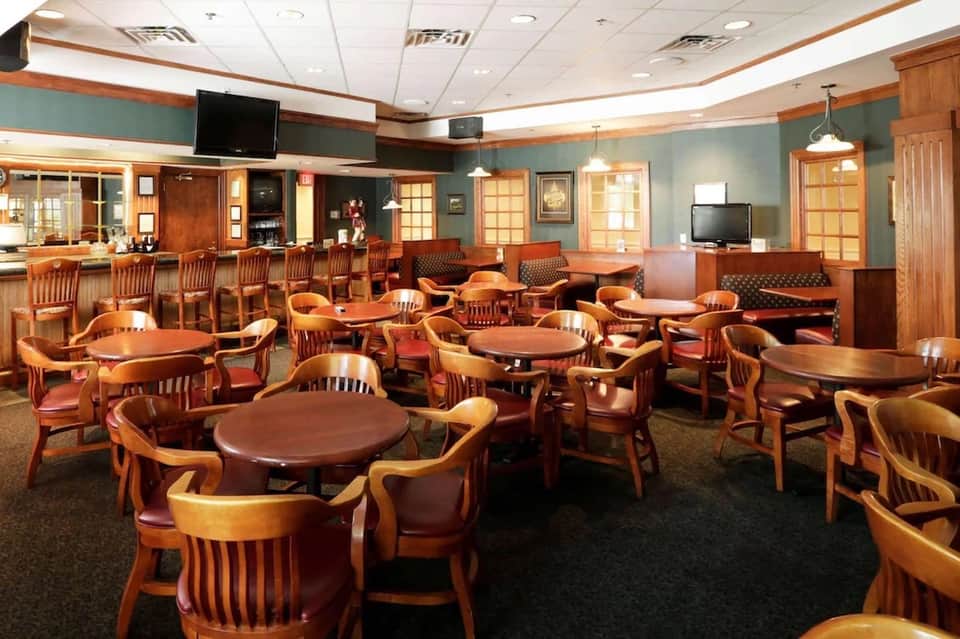 Hotel common area with wooden furniture, bar seating, green walls, and TV displays