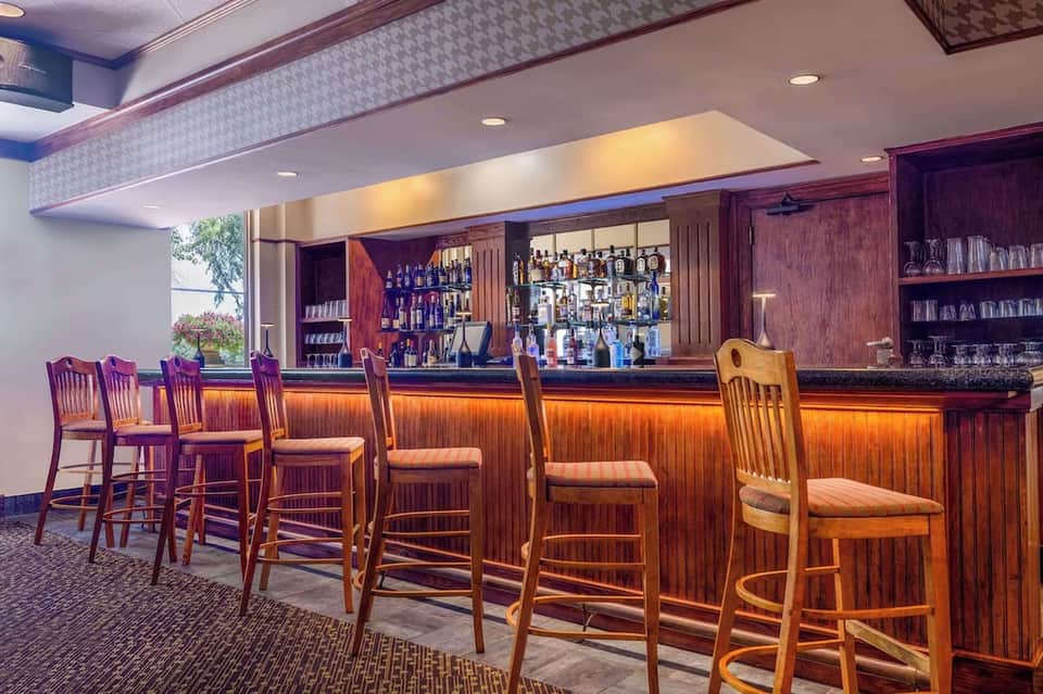 Hotel bar with wooden paneling, bar stools, and illuminated shelves of liquor bottles