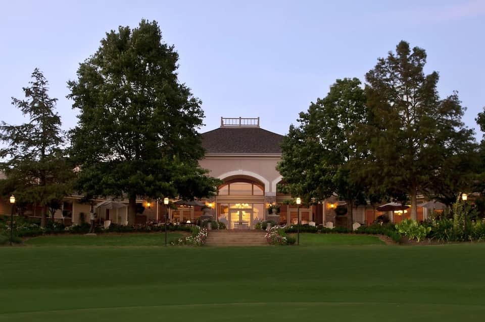 Elegant estate building at dusk with manicured lawn, arched entrance, and landscape lighting