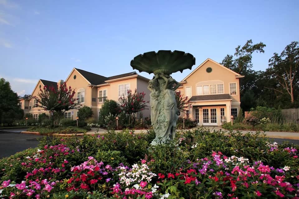 Luxury residential home with yellow exterior, manicured landscaping, and decorative fountain in front garden