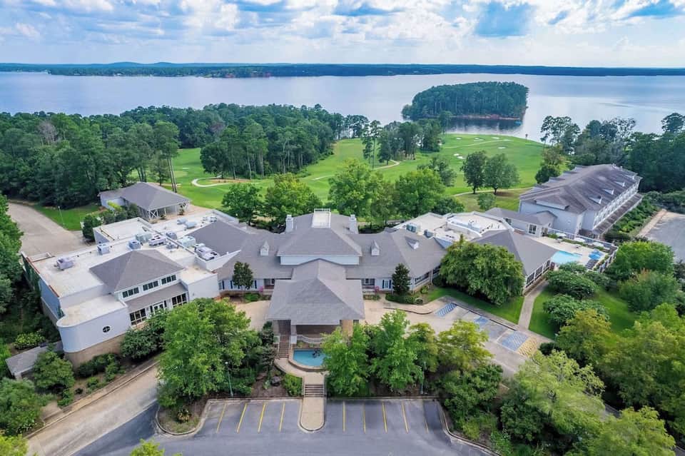 Aerial view of waterfront mansion with pool, manicured grounds, golf course, and lake views