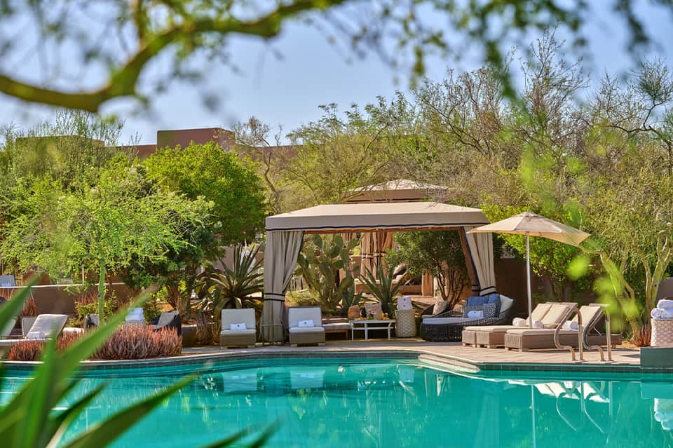 Luxury pool cabana with white curtains, loungers, and desert landscape views