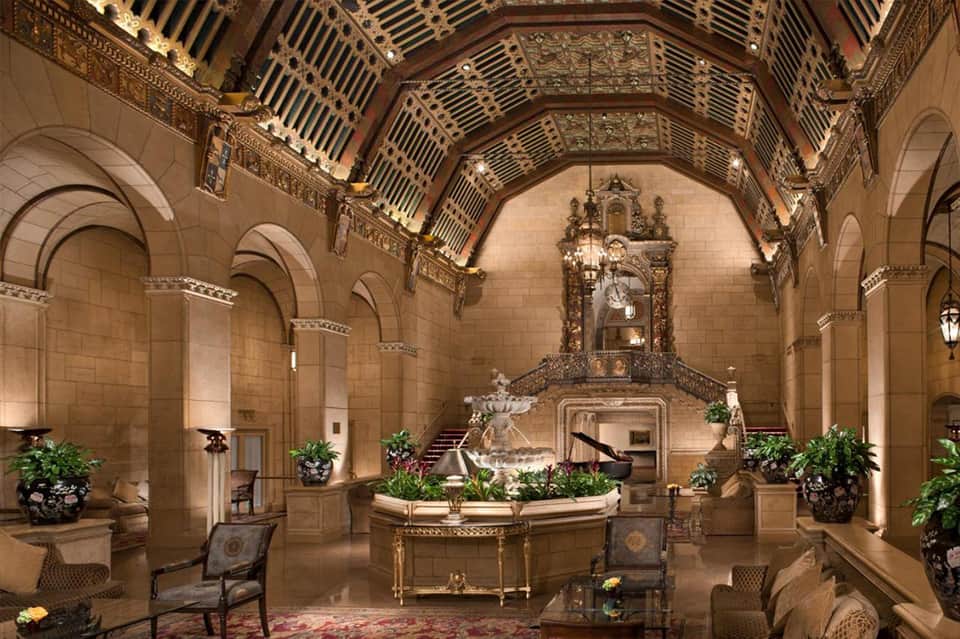 Grand historic hotel lobby with ornate coffered ceiling, arched columns, and decorative plants