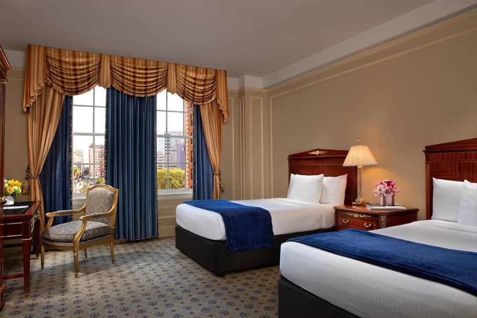 Luxury hotel room with two beds, elegant drapes, and city view from windows