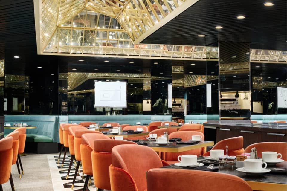 Modern hotel dining room with orange curved chairs, black tables, and large windows