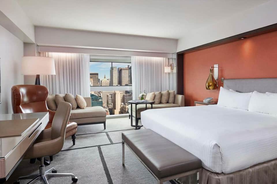 Luxury hotel suite with city skyline view, king bed, lounge seating, and orange accent wall