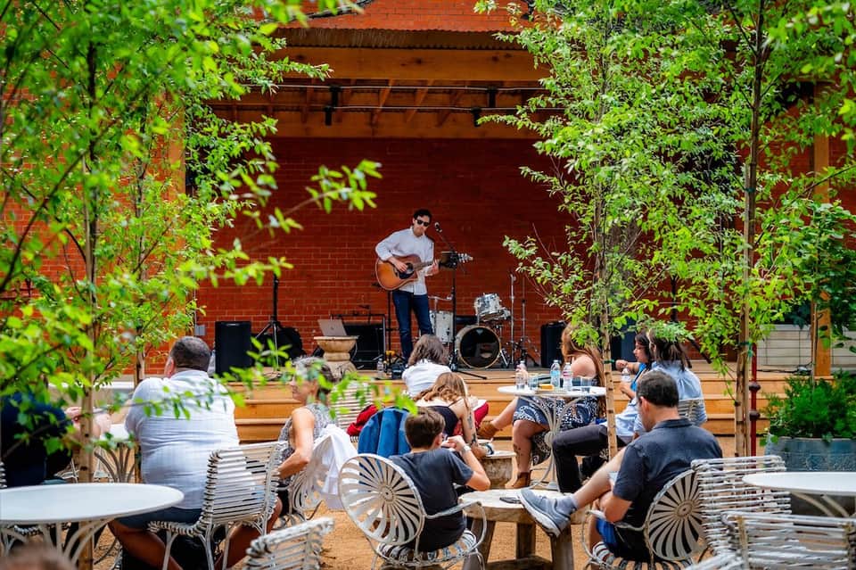 Live musician performing guitar for outdoor audience under red brick building