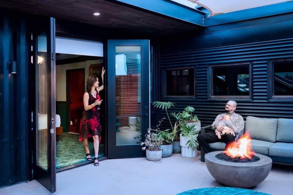 Modern patio with fire pit, gray seating, indoor-outdoor doors, and blue corrugated walls