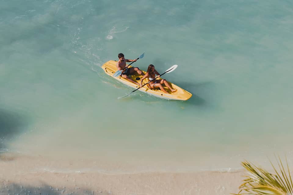 Couple kayaking in turquoise shallow water near sandy beach with palm trees