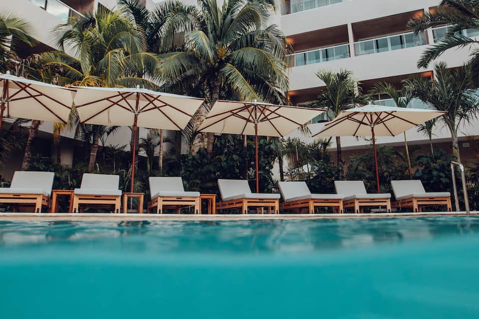 Modern hotel pool with white lounge chairs, umbrellas, and palm trees