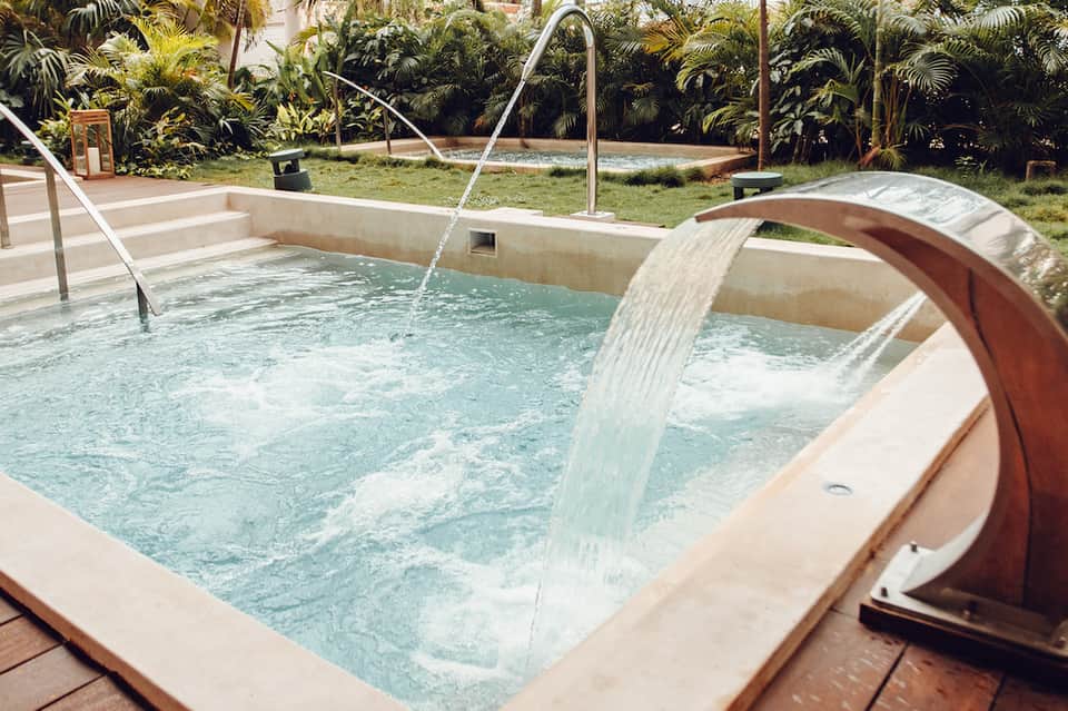 Outdoor hot tub with water feature and palm trees in a spa garden setting