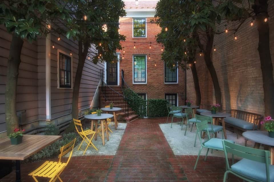 Brick courtyard with yellow and green chairs, string lights, and ivy-covered brick buildings