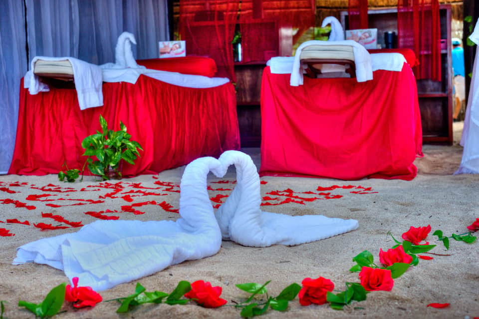 Beach wedding setup with white towel swans, red rose petals, and draped red and white fabric decorations