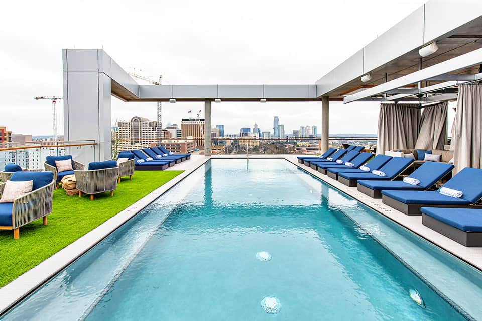 Rooftop infinity pool with city skyline view, blue loungers, and modern architectural elements