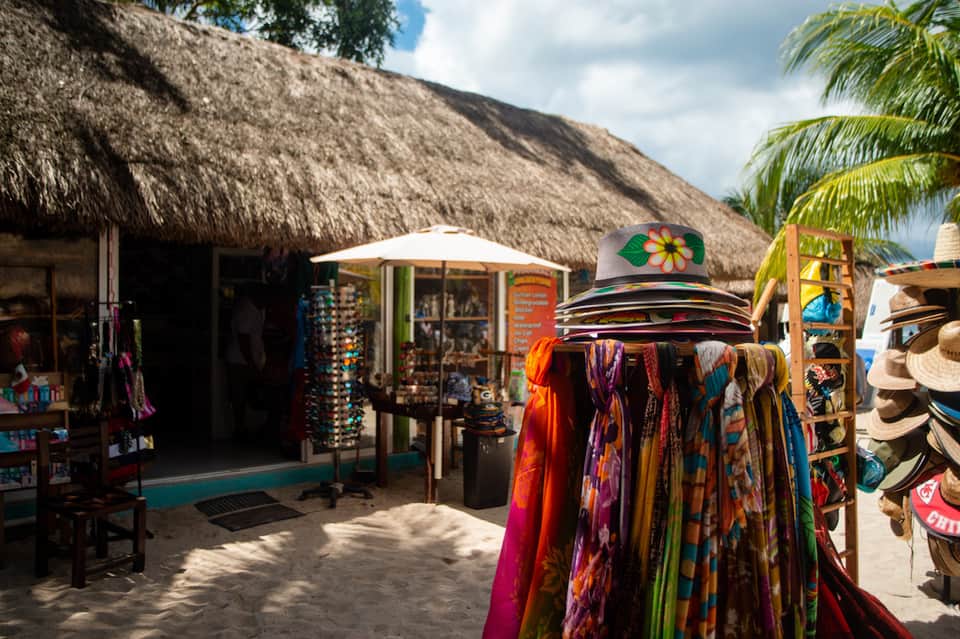 Beach market stall with colorful clothing, hats, and souvenirs displayed under thatched roof
