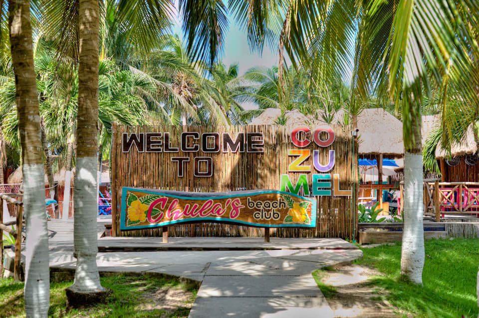 Tropical beach club entrance sign reading 'Welcome to Zu Mel' surrounded by palm trees