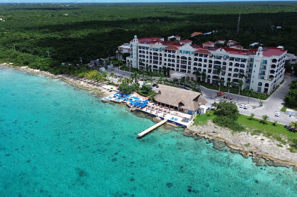 Aerial view of turquoise beachfront resort with red-roofed building and tropical trees