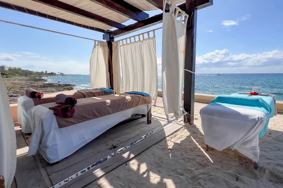 Beachside cabana with canopy bed, ocean views, and spa massage table on sandy beach