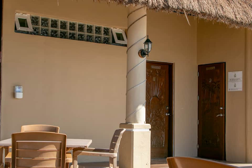 Covered outdoor patio area with wooden doors, lantern, and furnished seating with thatched roof