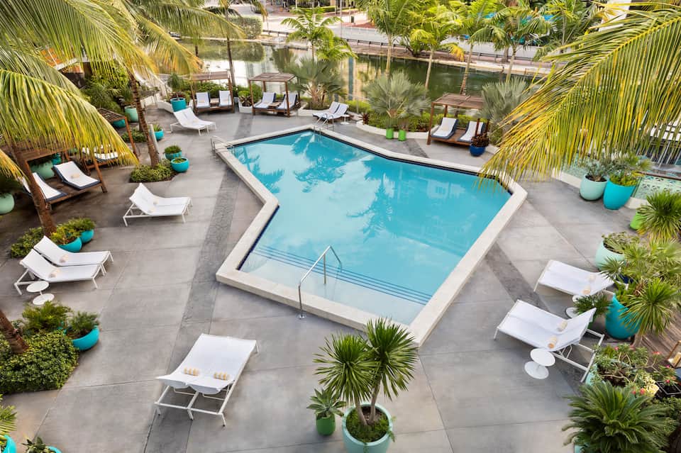 Resort pool deck with turquoise pool, white loungers, and tropical palm trees