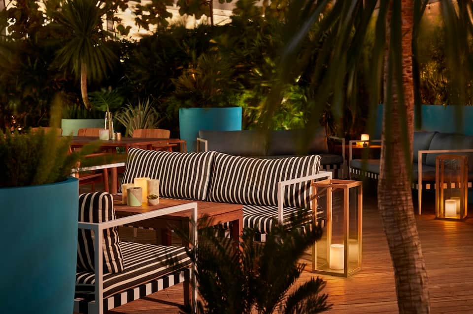Outdoor lounge area at night with striped seating, potted plants, and ambient lighting