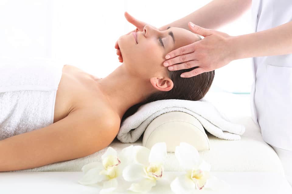 Woman receiving head massage at spa with white orchids and towels in relaxing setting