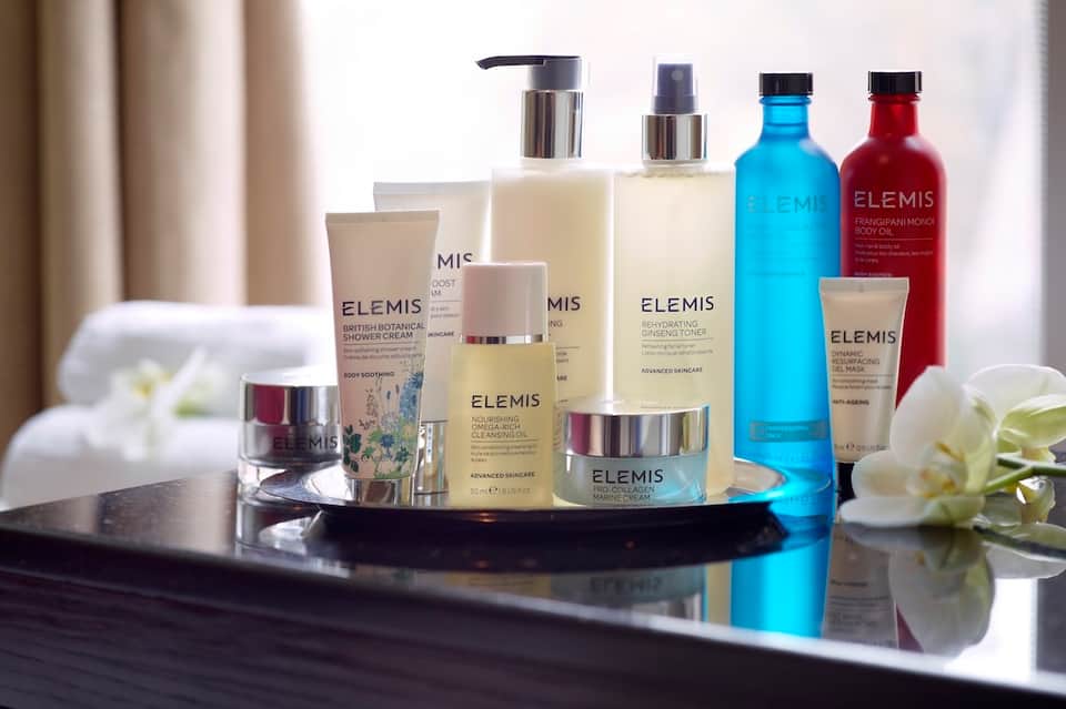Luxury skincare product collection including ELEMIS brand bottles and jars displayed on reflective surface