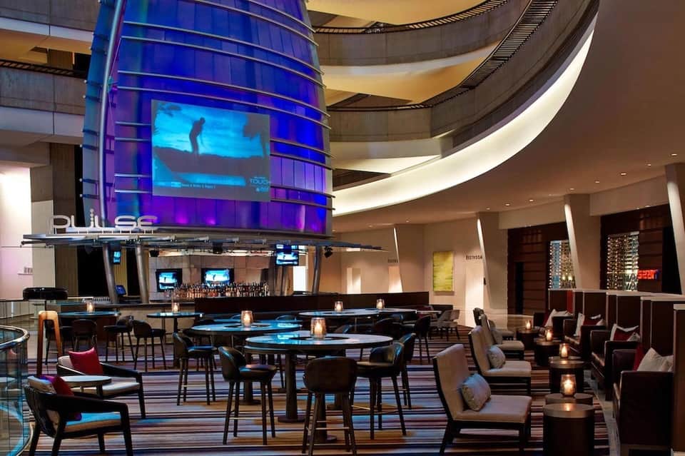 Modern hotel lounge with blue-lit bar, circular seating, and digital display screens