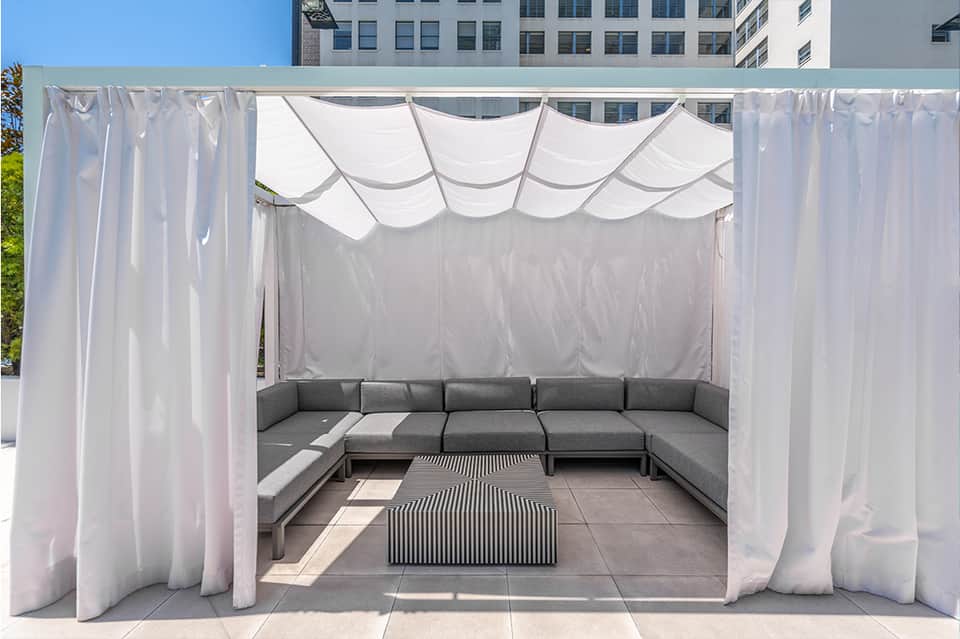 Outdoor cabana with white sheer curtains and gray sectional sofa on rooftop terrace