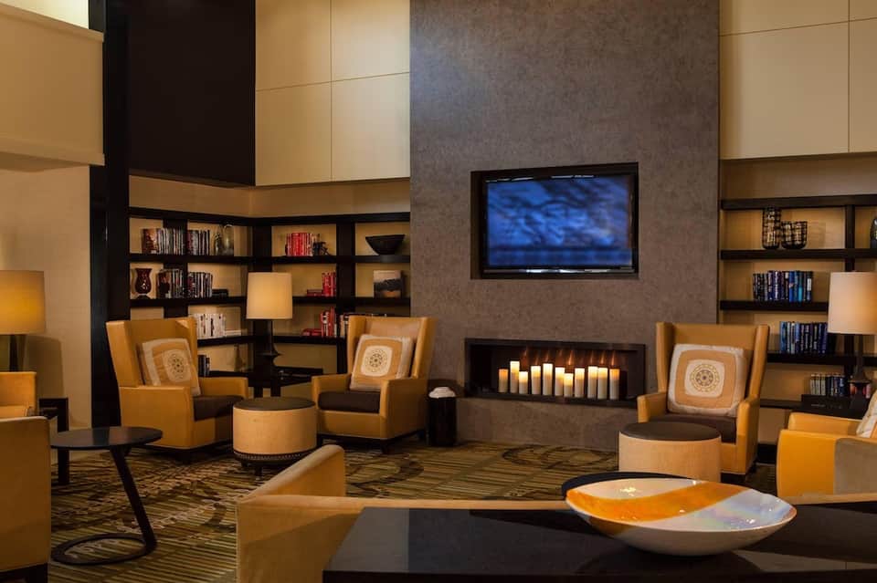 Upscale lounge with fireplace, candles, tan armchairs, built-in bookshelves, TV, and modern décor