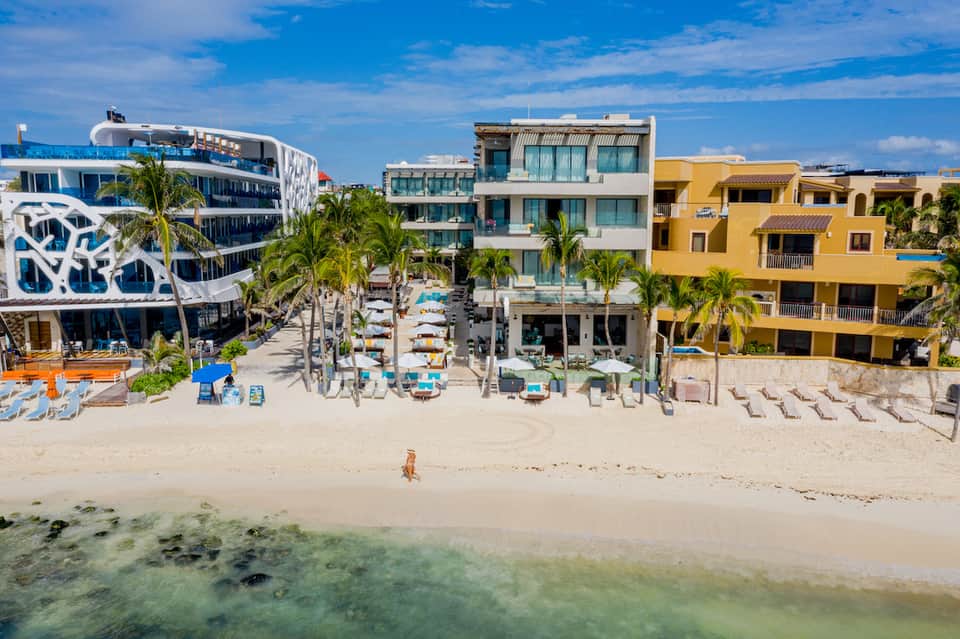 Colorful beachfront resort buildings with sandy beach, blue water, and lounge chairs under umbrellas