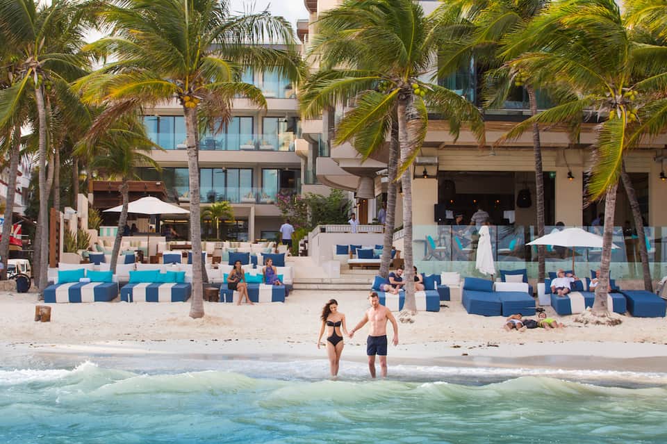 Modern beachfront resort with blue and white lounge seating, palm trees, and ocean view
