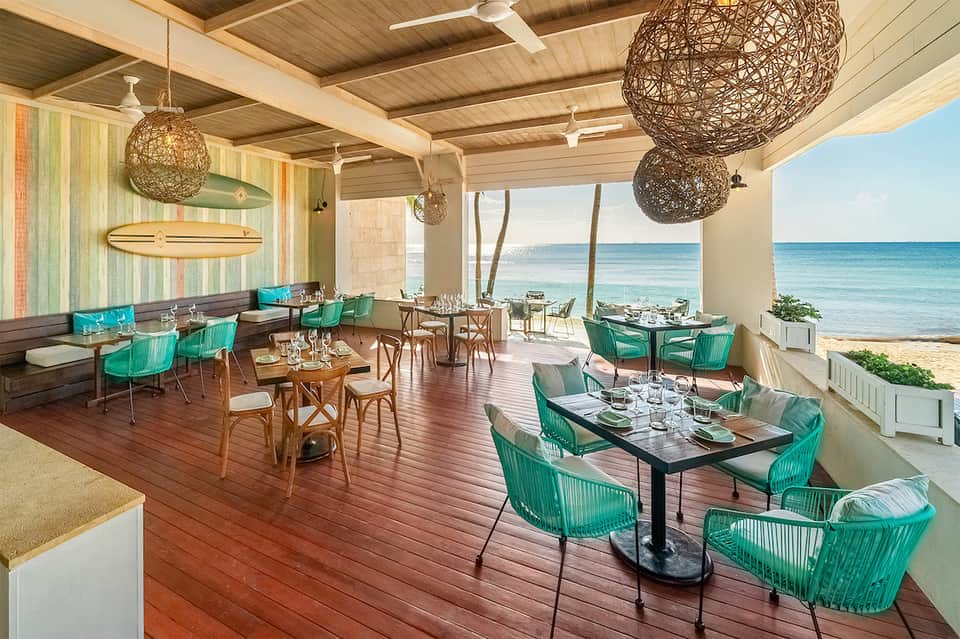 Modern beachfront restaurant with green chairs, wood ceiling, and ocean views