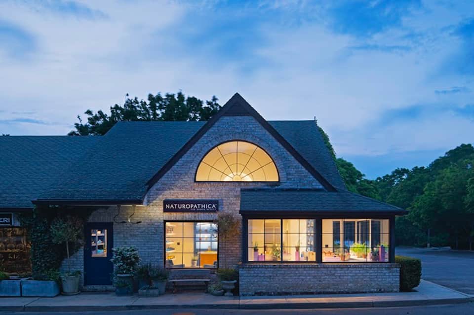 Naturopathica spa storefront with brick facade and illuminated signage at dusk
