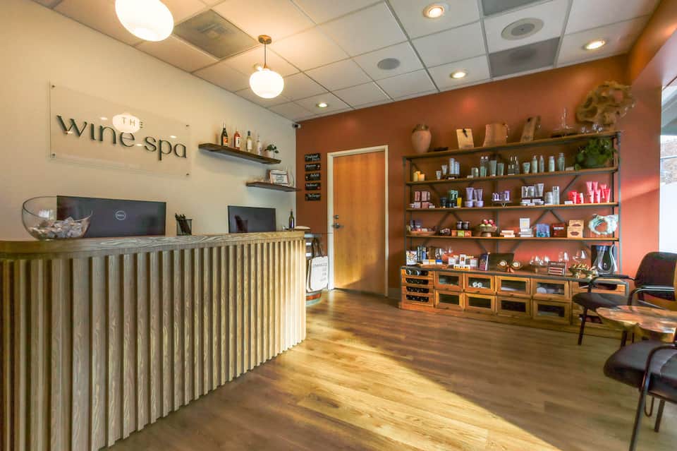 Wine spa reception desk with wooden counter, orange accent walls, and shelving displaying products