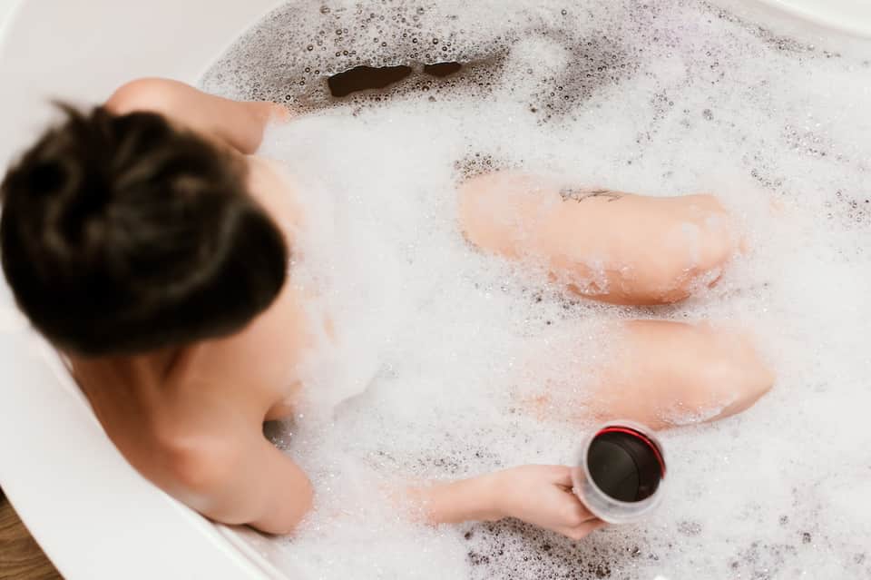 Child's hands playing in bubble bath with soap suds and holding a cup