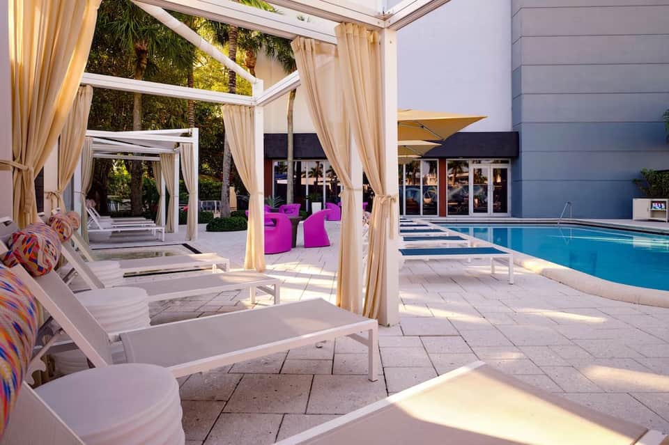 Luxurious pool area with white cabanas, cream curtains, and modern resort architecture