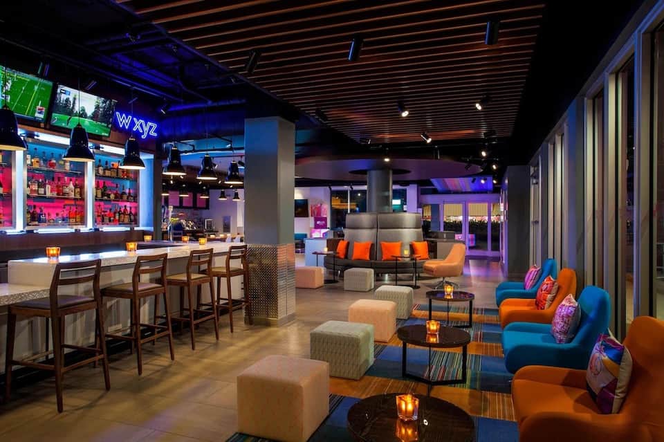 Modern hotel lounge with colorful seating, bar area, blue ambient lighting, and open concept