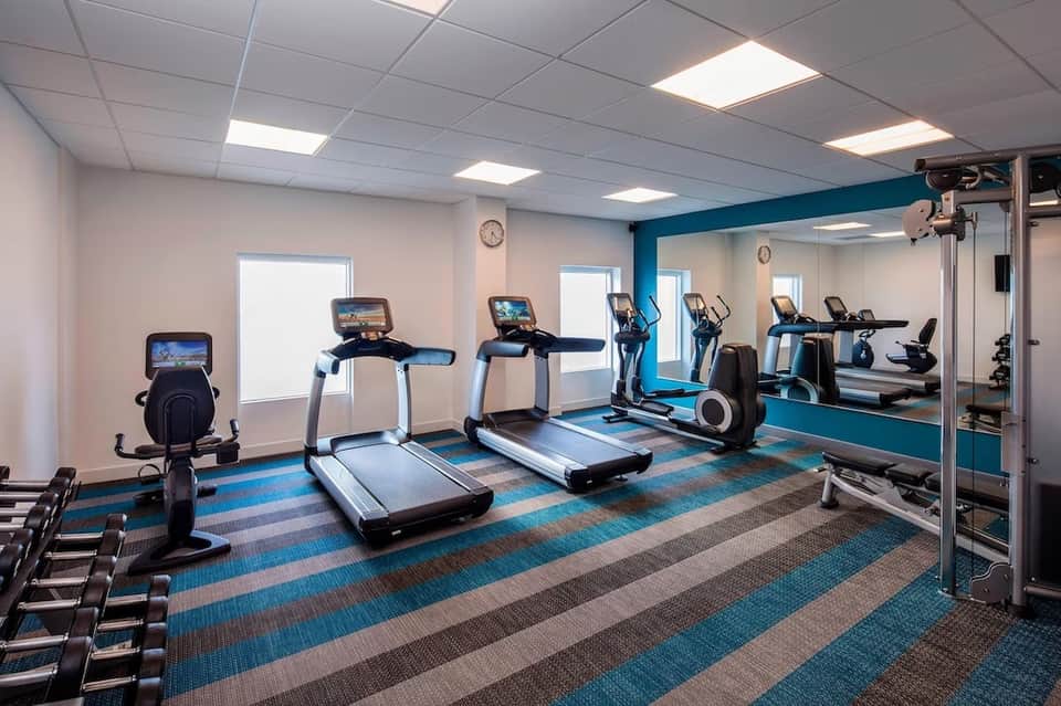 Contemporary fitness center with treadmills, exercise bikes, and mirrored walls with blue accents