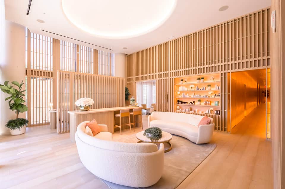 Modern spa lounge with curved seating, wooden lattice walls, orange accents, and skylight ceiling