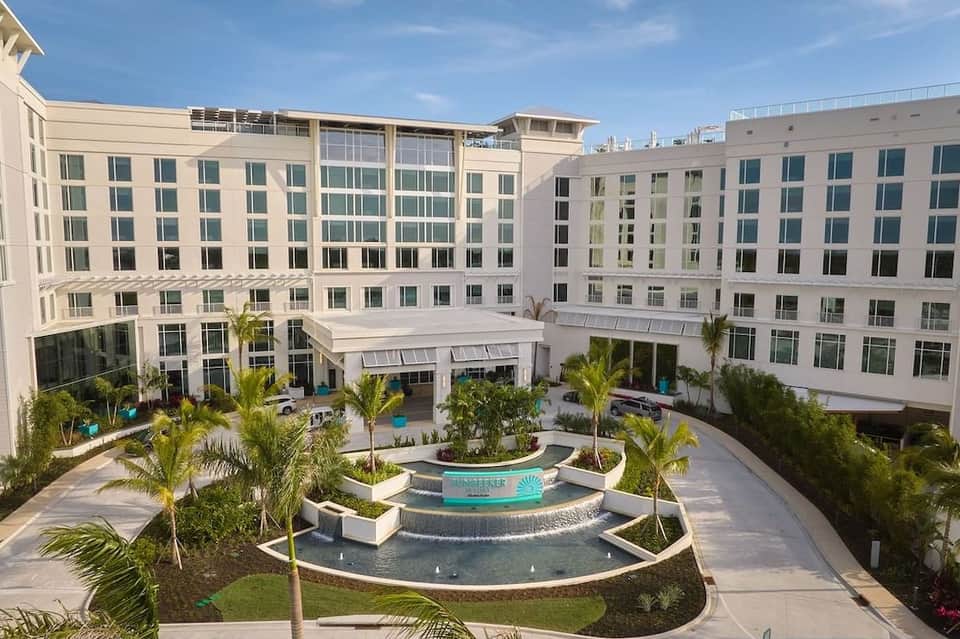 Modern hotel courtyard with fountain, palm trees, and surrounding multi-story buildings
