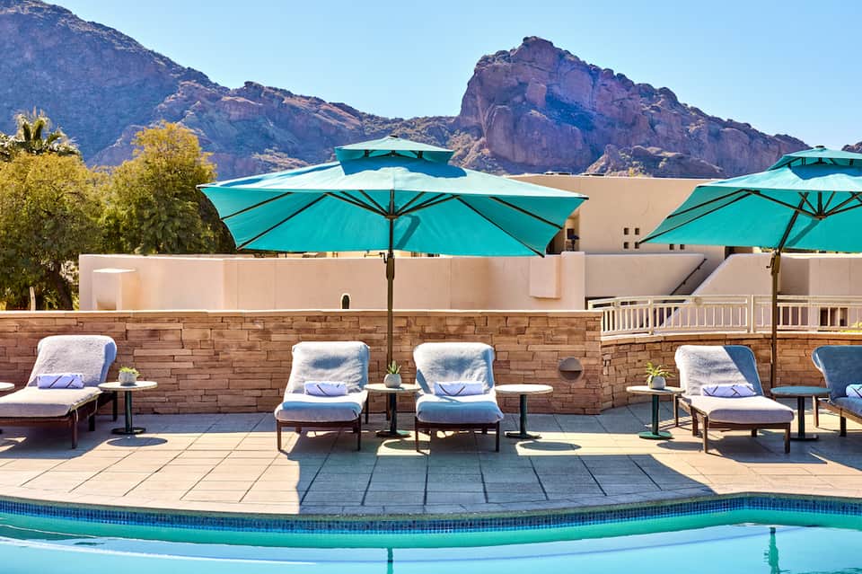 Turquoise umbrellas over lounge chairs by pool with dramatic red rock mountains in background