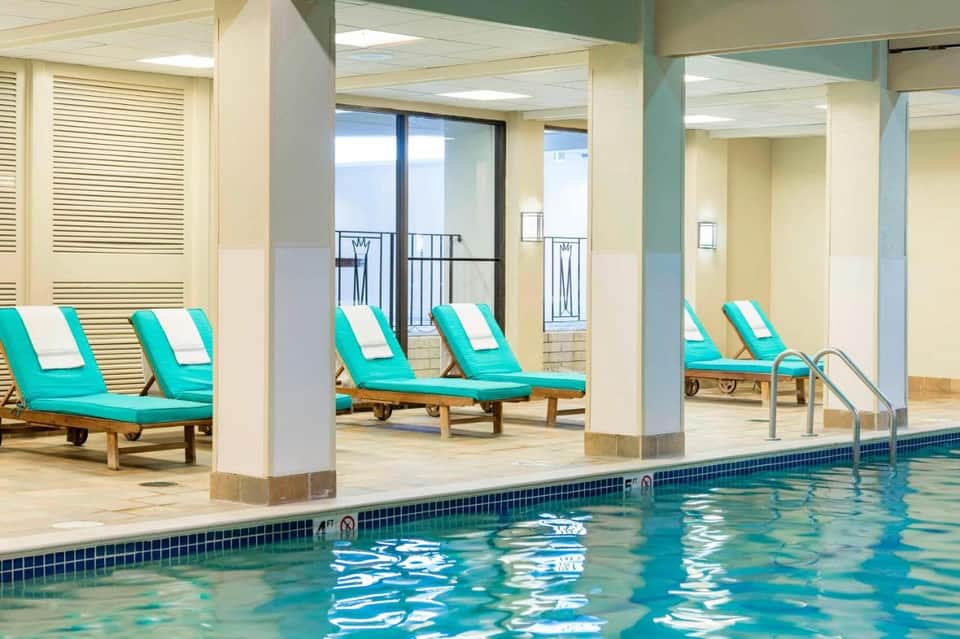 Indoor pool area with turquoise lounge chairs and white pillows under exposed ceiling beams