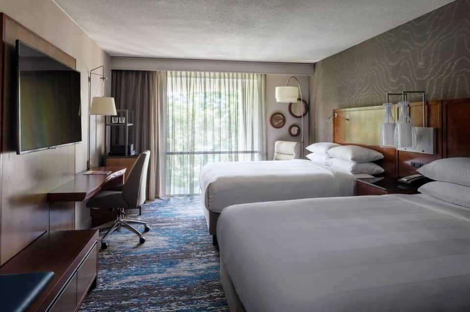 Modern hotel room with two queen beds, desk, TV, and sliding glass doors to balcony