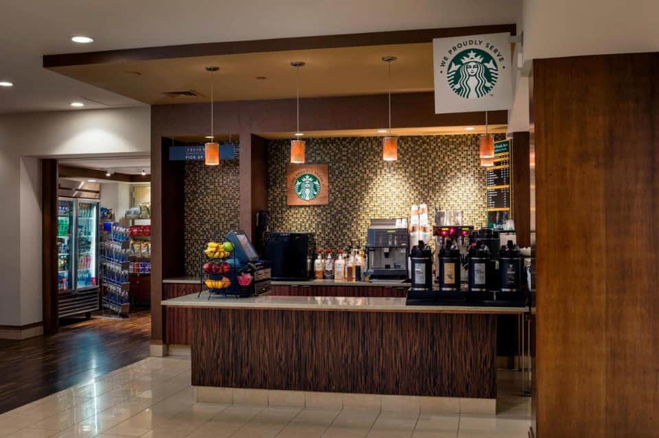 Starbucks café counter with espresso machines, merchandise, and ambient lighting in hotel lobby