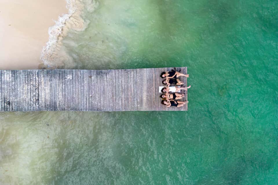 Aerial view of people relaxing on wooden pier over turquoise tropical ocean water