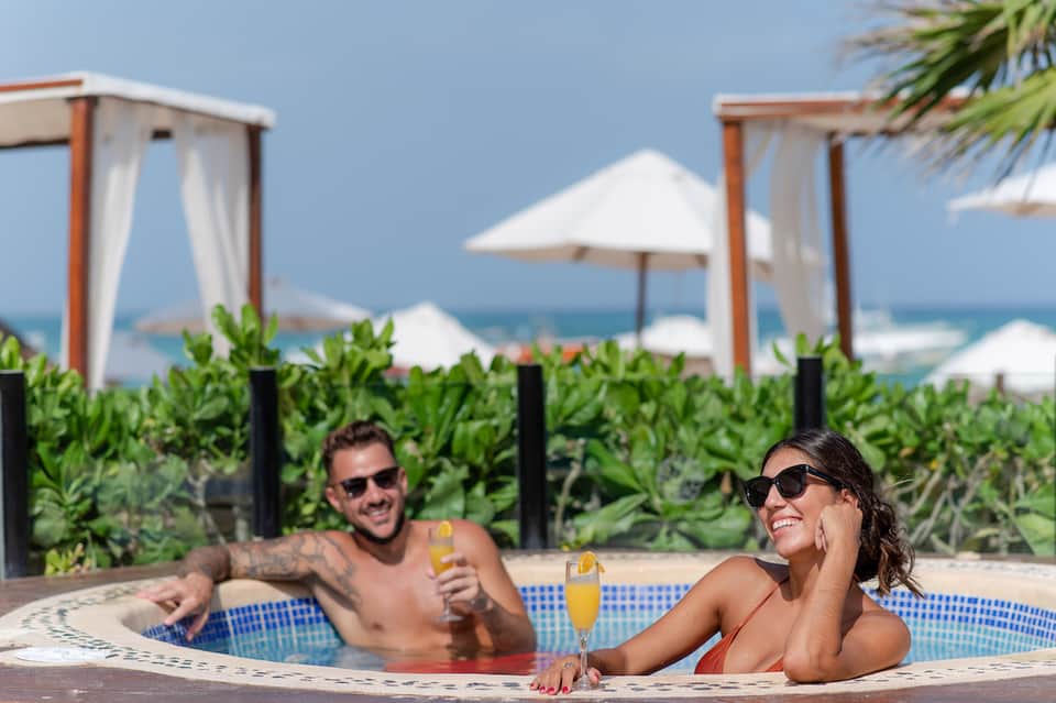 Couple relaxing in hot tub with ocean views, surrounded by white umbrellas and tropical vegetation